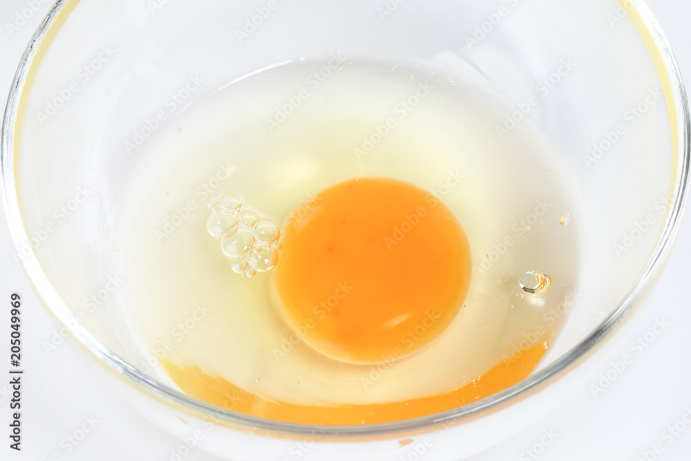 Raw Egg Yolk and white liquid in transparent glass bowl white background Raw Egg Yolk and white liquid in transparent glass bowl white background