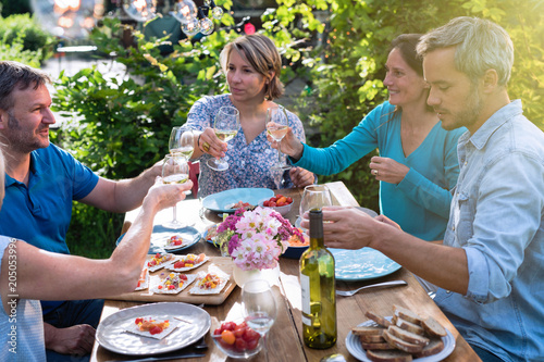 Group of friends gathered around a table in a garden on a summer evening to share a meal and have a good time together