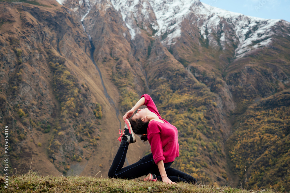young girl performs asanas yoga on the background of mountains