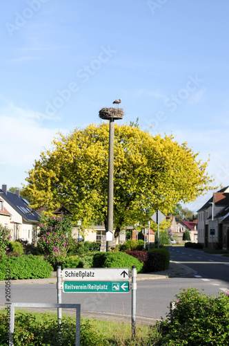 Dorfplatz mit Storchenhorst und Storch sowei Schild Reitplatz und Schießplatz photo