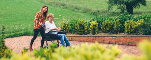 Konstfotografi Young woman carrying her mother in a wheelchair through the garden
