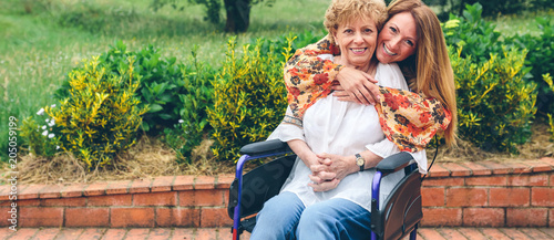 Daughter embracng her senior mother in wheelchair in the garden