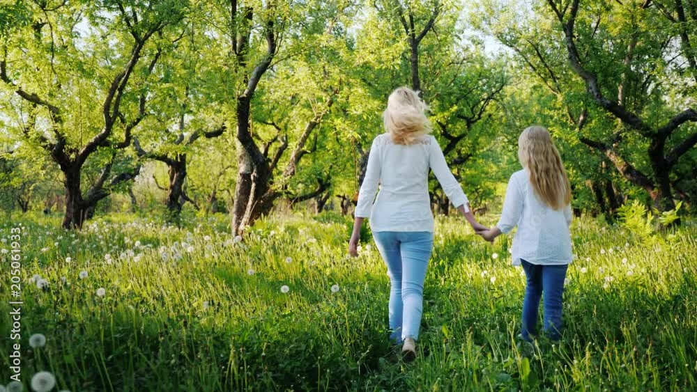 Mom and daughter are walking in the apple garden, enjoying the warm spring day Mom and daughter are walking in the apple garden, enjoying the warm spring day