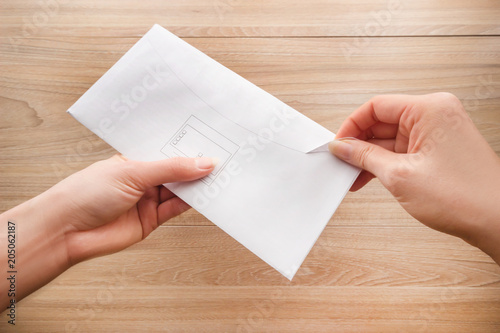 Woman's hand holds and opens a white paper envelope or letter envelopes on a wooden desk top view background.