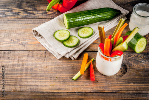 Summer healthy snack appetizer, assorted colorful fresh vegetable sticks (celery, rhubarb, pepper, cucumber and carrot) with yoghurt sauce dip, wood and dark concrete background copy space