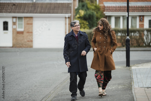 Mature couple are talking and laughing as they walk down the residential street together. 