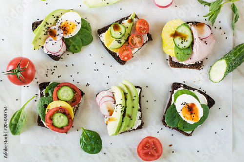 Different sandwiches with vegetables, eggs, avocado, tomato, rye bread on light marble table. Top vew. Appetizer for party. Flat lay.