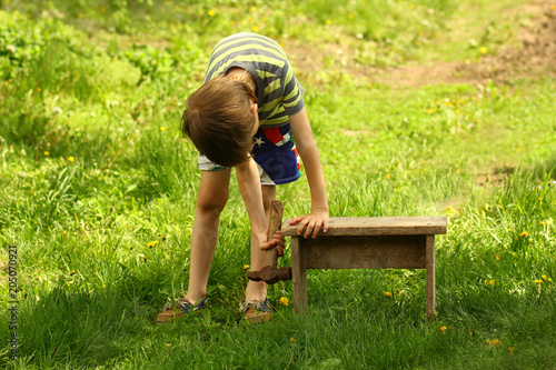 Boy repairing wooden bench with a hammer in the back yard