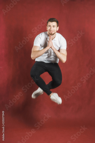 Photo of a young man on a red wall background looking at camera jumping. © Виталий Давыдов