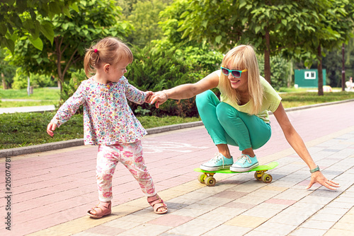 Beautiful smiling emotional mother with her daughter riding a skateboard in the park. Ekstrim photo