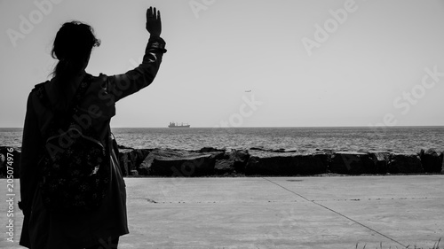 Quadro em tela The silhouette of a sad woman or girl standing alone on the seaside and waving her hand to the distant ship with feeling lonely