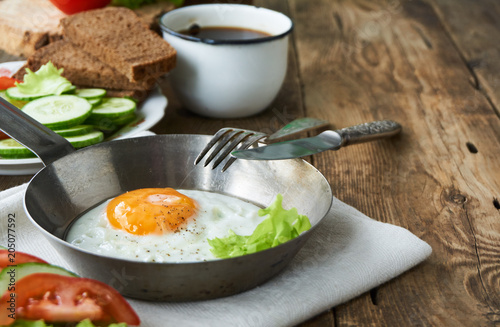 Fried egg in a frying pan with vegetables on a wooden table            