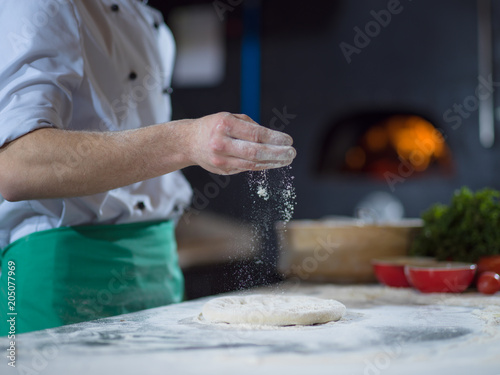 chef sprinkling flour over fresh pizza dough