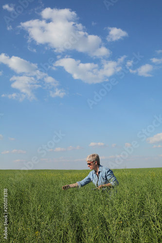 Female agronomist or farmer examining green canola field, rapeseed plant in spring