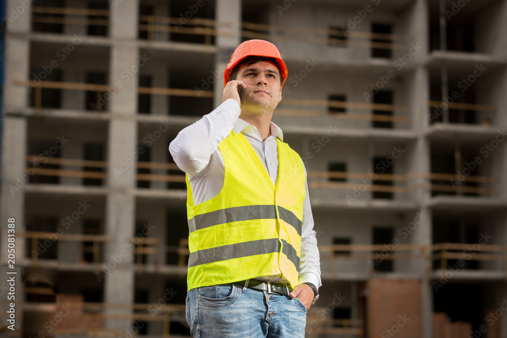 Portrait of young confident man in white shirt and protective helmet talking by phone on building site Portrait of young confident man in white shirt and protective helmet talking by phone on building site
