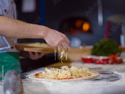 chef sprinkling cheese over fresh pizza dough