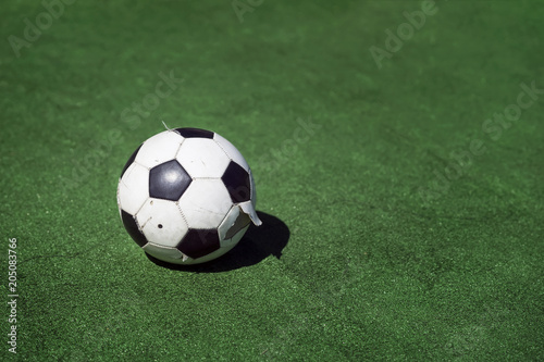Old, dirty tattered soccer ball on background of green grass. Traditional classic black and white football ball on green field of stadium training, playground, copy space