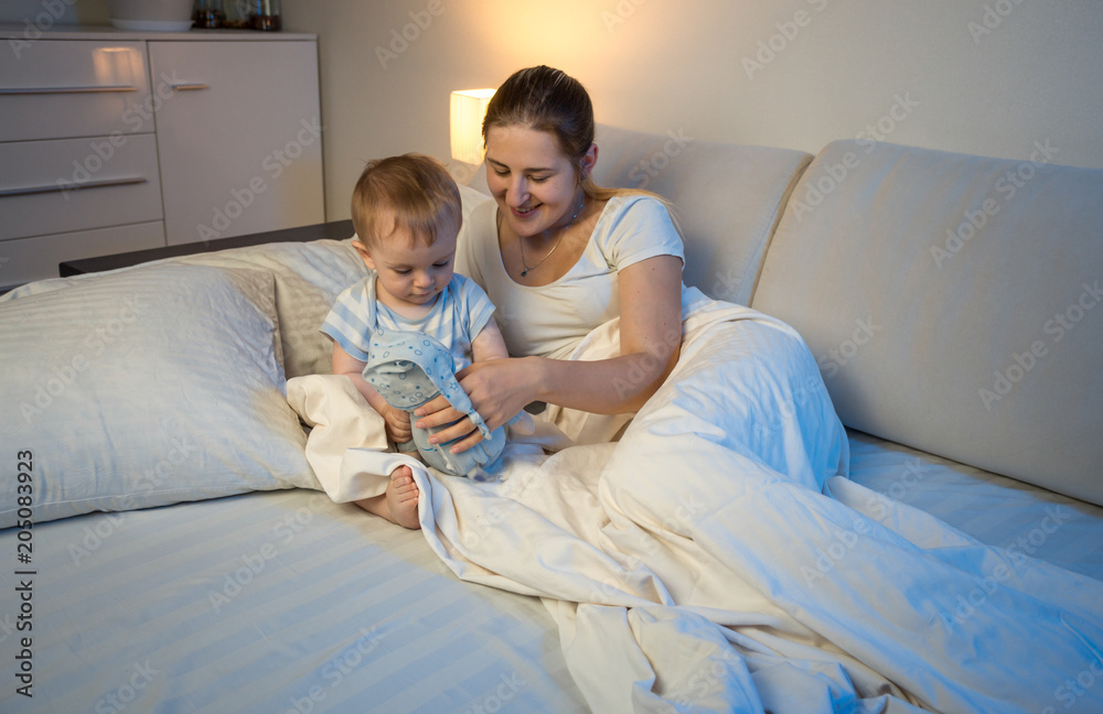 Young mother with baby boy lying in bed and playing with toy Young mother with baby boy lying in bed and playing with toy