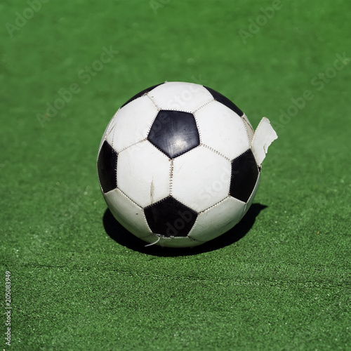 Old, dirty tattered soccer ball close-up. Traditional classic black and white football ball on green field of stadium training, playground. Square