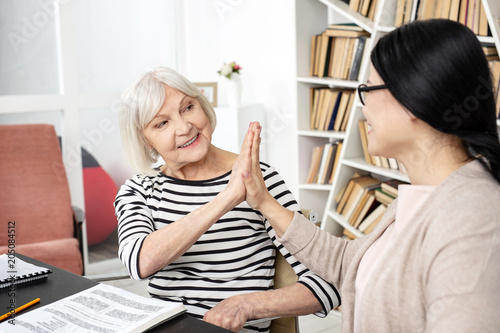 Be proud. Optimistic mature tutor and woman exchanging high five while smiling photo