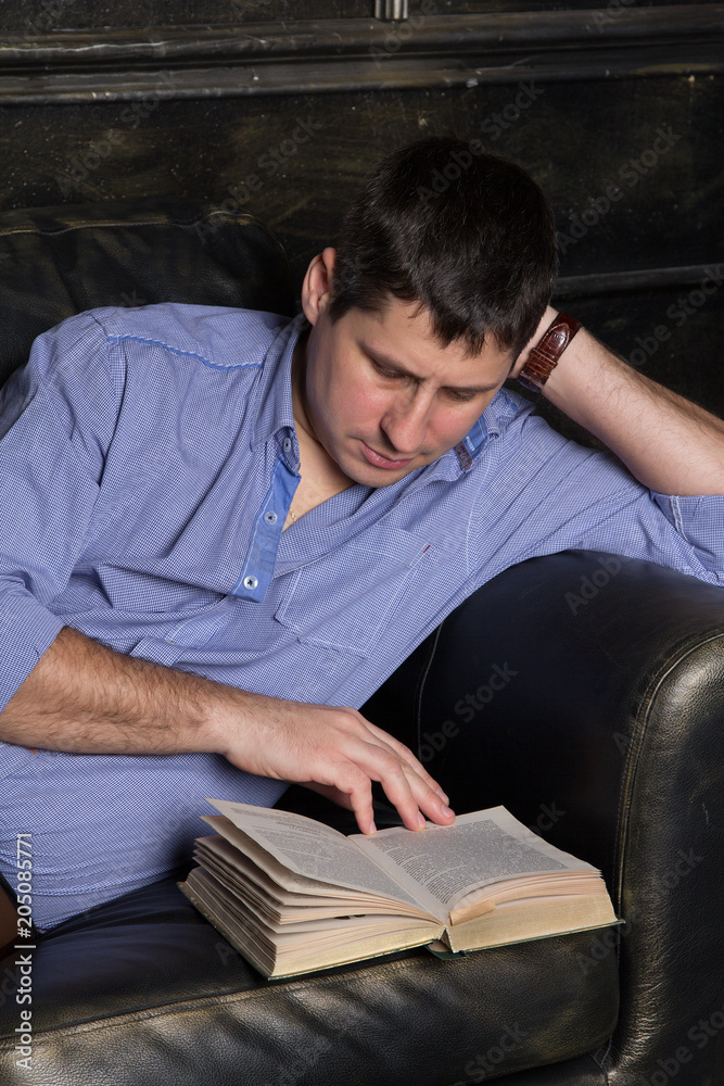 Young man is lying on the sofa and is reading a book. Close-up.