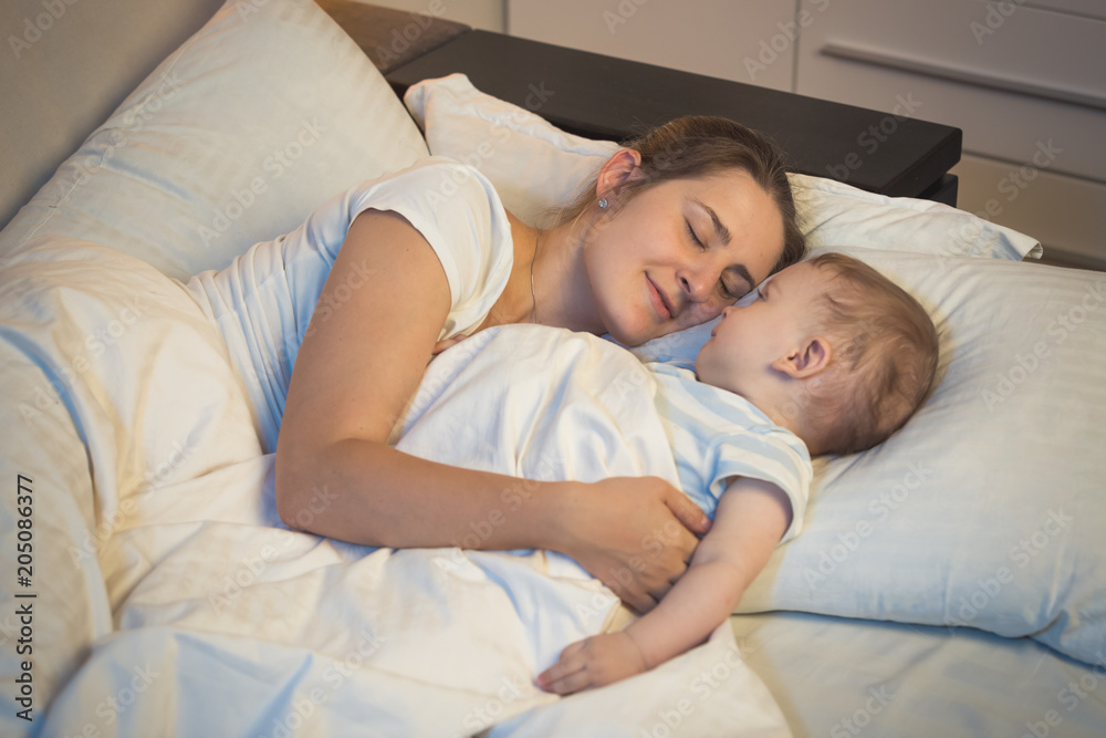 Toned portrait fo young mother sleeping in bed with her 9 months old baby son Toned portrait fo young mother sleeping in bed with her 9 months old baby son