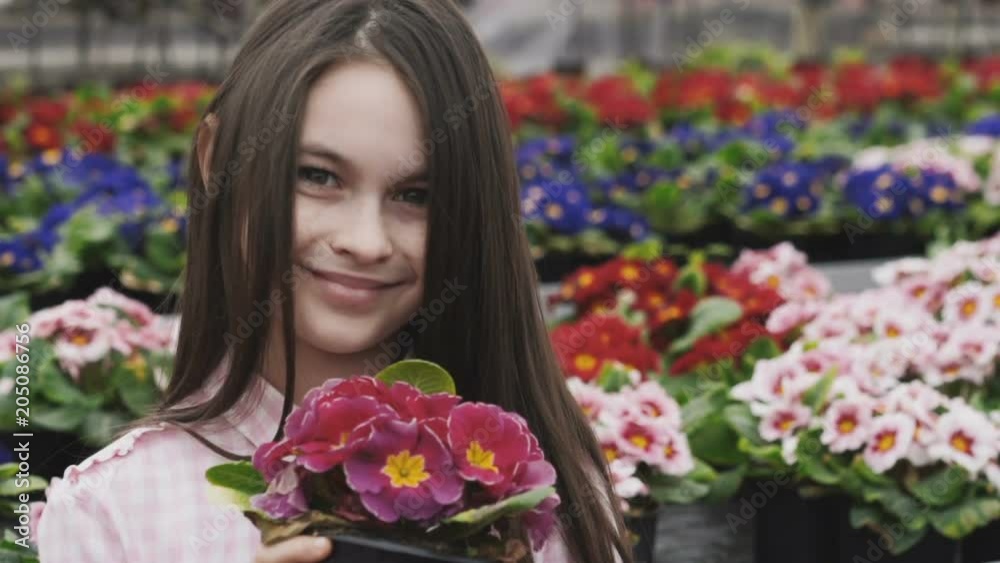 Pretty girl smells flowers with smile, poses and looks at camera Pretty girl smells flowers with smile, poses and looks at camera