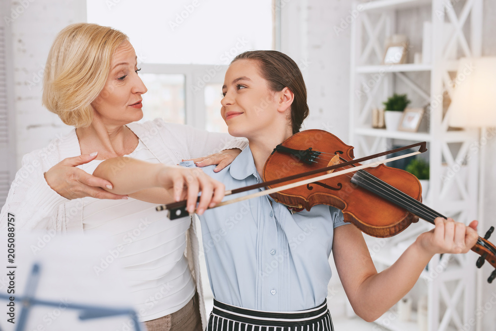 Docile player. Cheerful brunette looking at her tutor while playing the violin Docile player. Cheerful brunette looking at her tutor while playing the violin