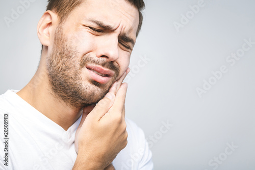 Toothache. Handsome young man suffering from toothache, closeup, touching his cheek to stop pain against white background. Strong toothache photo