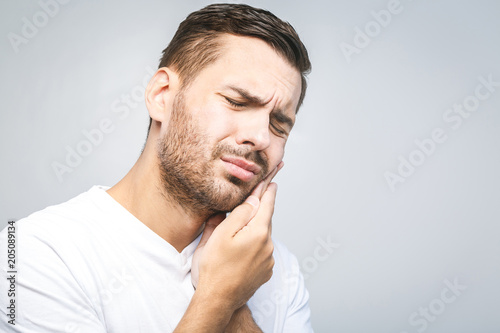 Toothache. Handsome young man suffering from toothache, closeup, touching his cheek to stop pain against white background. Strong toothache photo