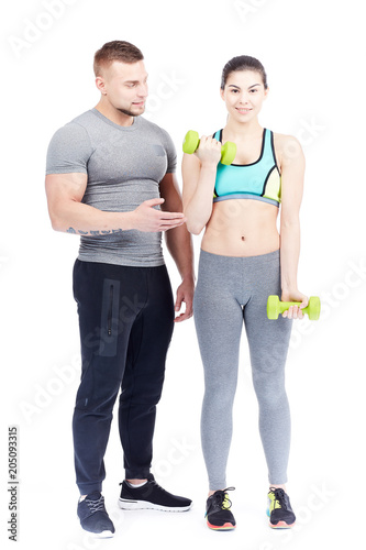 Male fitness instructor assisting fit young woman doing dumbbell exercise
