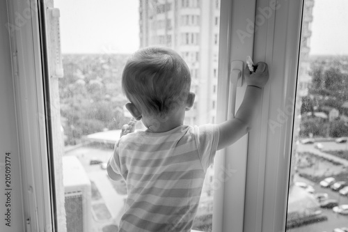 Black and white image of baby pulling window handle and trying to open it