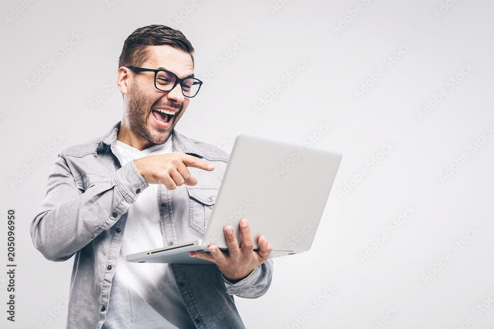 Funny young handsome man in shirt holding laptop and smiling while standing against white background. Have fun. Funny young handsome man in shirt holding laptop and smiling while standing against white background. Have fun.