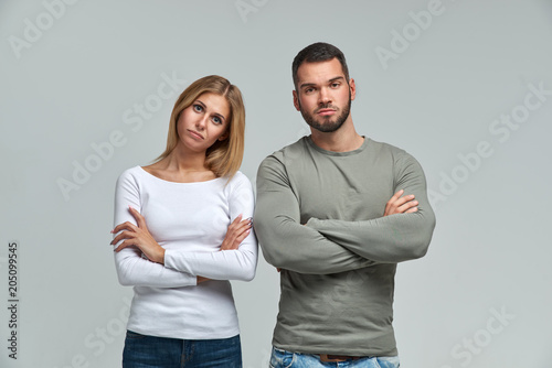 Studio portrait of young beautiful couple with unhappy faces and negative emotions stare into camera with hands folded on Breasts
