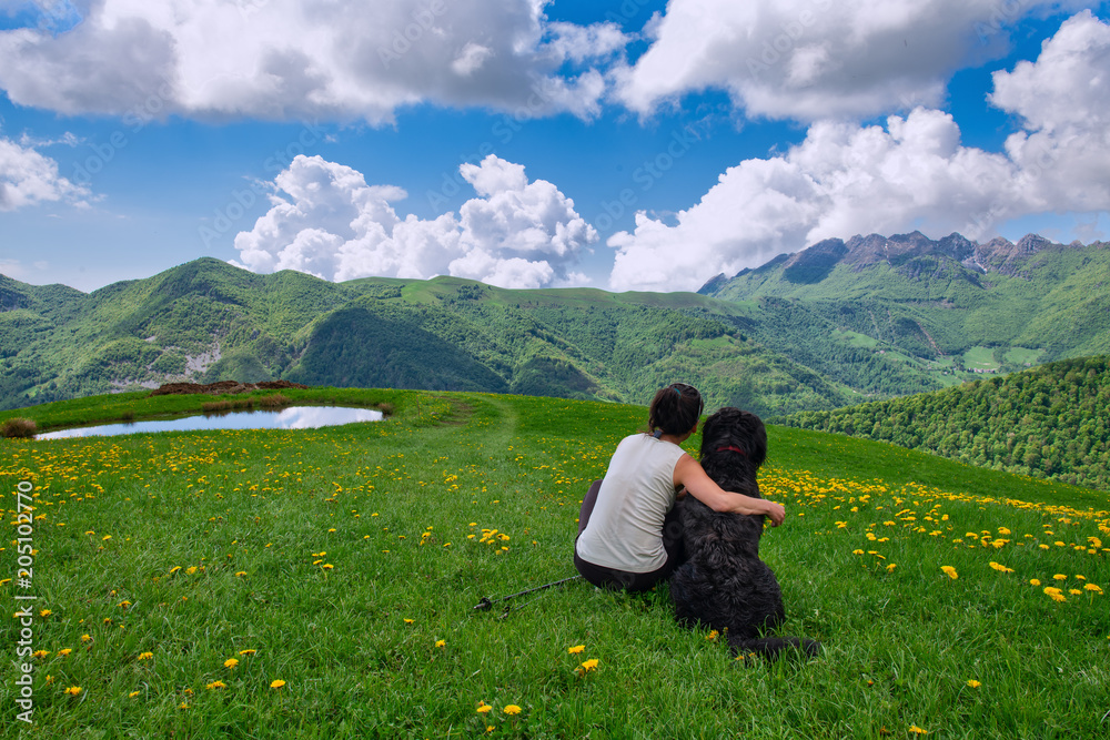 A girl with her big dog looks at the landscape in the mountains