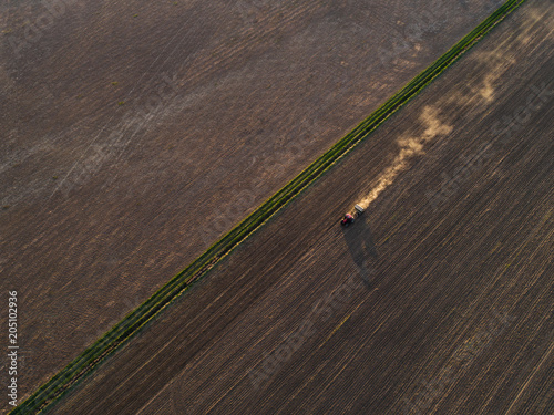 Aerial view of the tractor in the field, spring sowing work. Sowing of wheat in a field at sunset