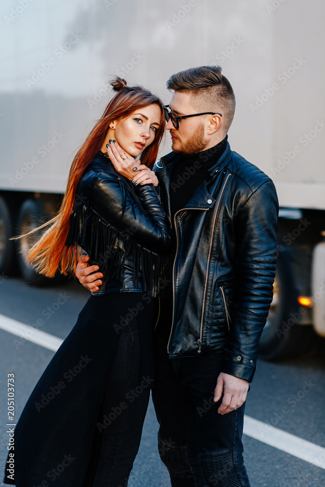 red skinny girl in a black dress stands together with the bearded guy on the highway
