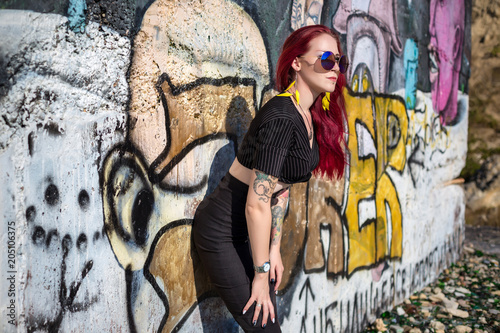sexy redhair woman in hooligan outfit and sunglasses posing against graffiti wall