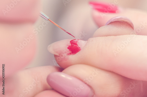 Manicurist paints nails with red lacquer in the salon