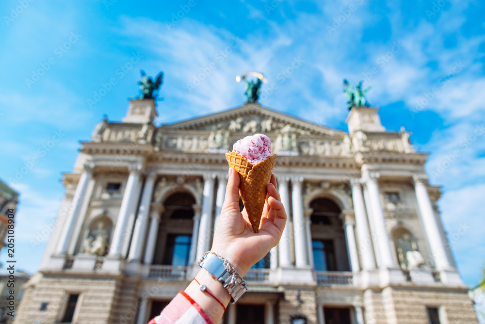 first-person view. woman hold ice cream in hand old european building on background