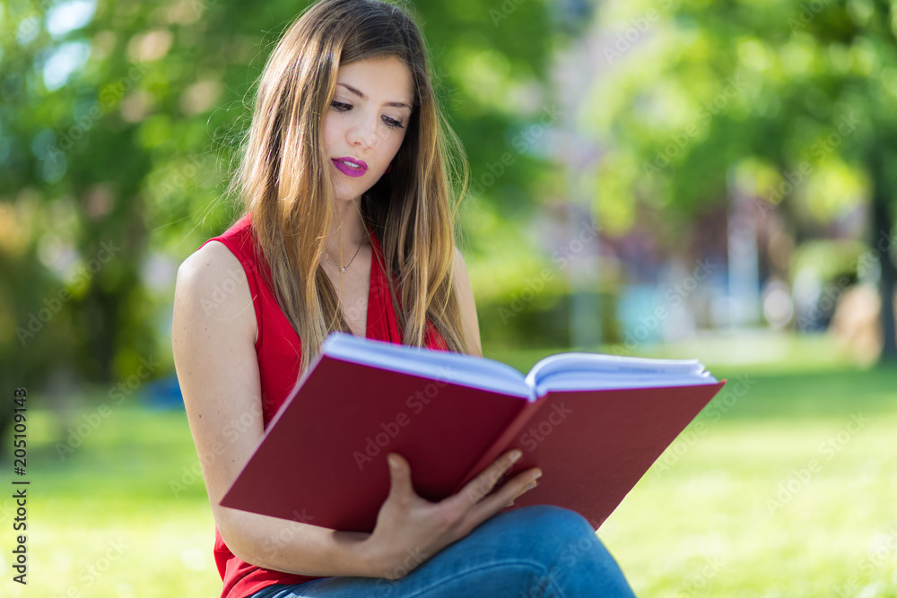 Young woman sitting in a park and reading a book Young woman sitting in a park and reading a book