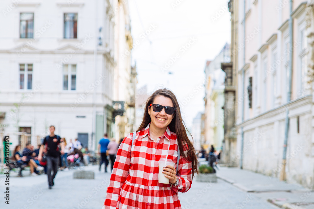 woman drinking cool drink while walking city street at summer day