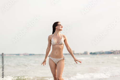 Woman in bikini walking down the beach in her summer vacation along the water © Kzenon