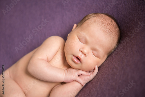 Naked newborn baby sleeping on purple background