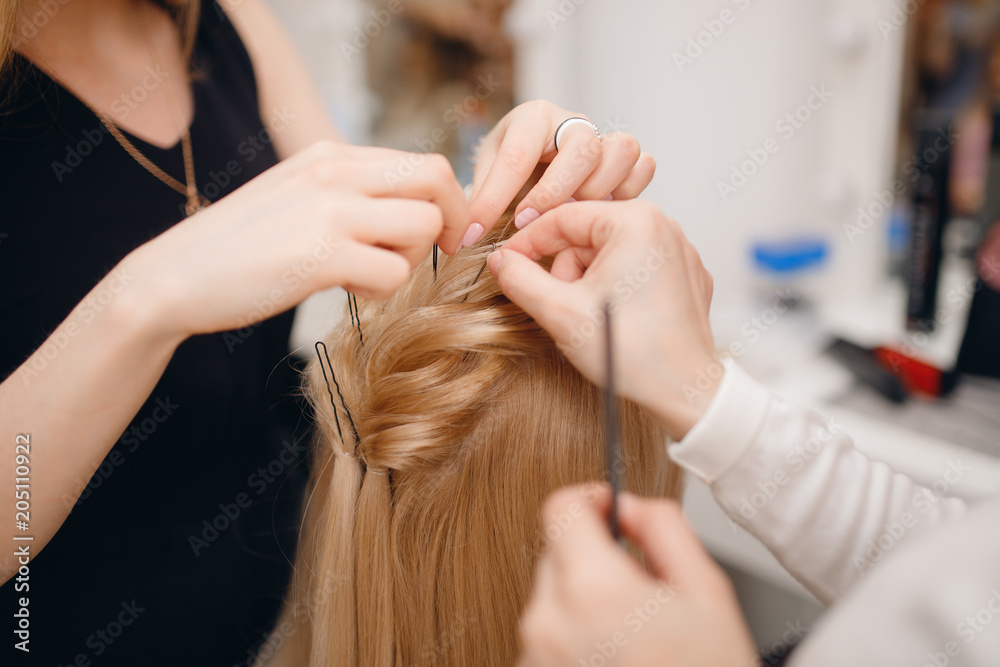 Naklejka premium Hairdresser woman conducts training for pupil in salon, weaving braid hair, wedding styling.