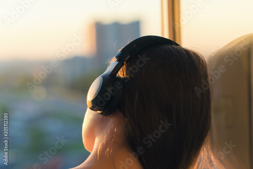 Girl in headphones listening to music in the city at sunset