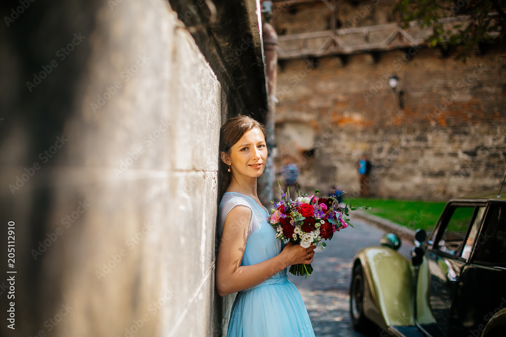 Obraz premium Beautiful young bride posing in a wedding blue dress in old street, 
