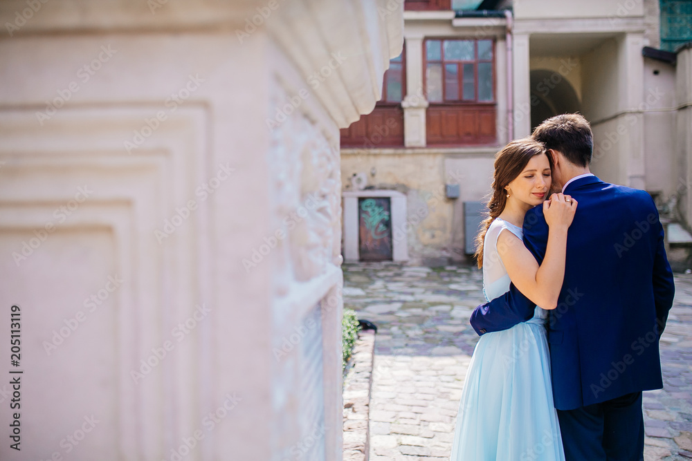 Portrait the groom in wedding suit and the bride in dress walking back near old building, old house outside, outdoor. Newlyweds are walking along the streets. Kissing couple. Wedding walks. Dancing. Portrait the groom in wedding suit and the bride in dress walking back near old building, old house outside, outdoor. Newlyweds are walking along the streets. Kissing couple. Wedding walks. Dancing.