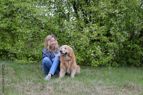 a girl  is sitting on the grass with  the Golden Retriever