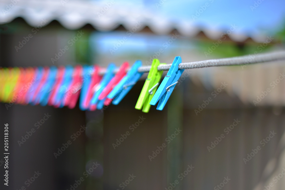 Fototapeta premium Color clothespins hang on the clothesline. laundry hook, colorful, pegs, rope ,outside, sun ,green, summer decorations, village, blue, sky , yellow ,red ,pins ,pink ,over